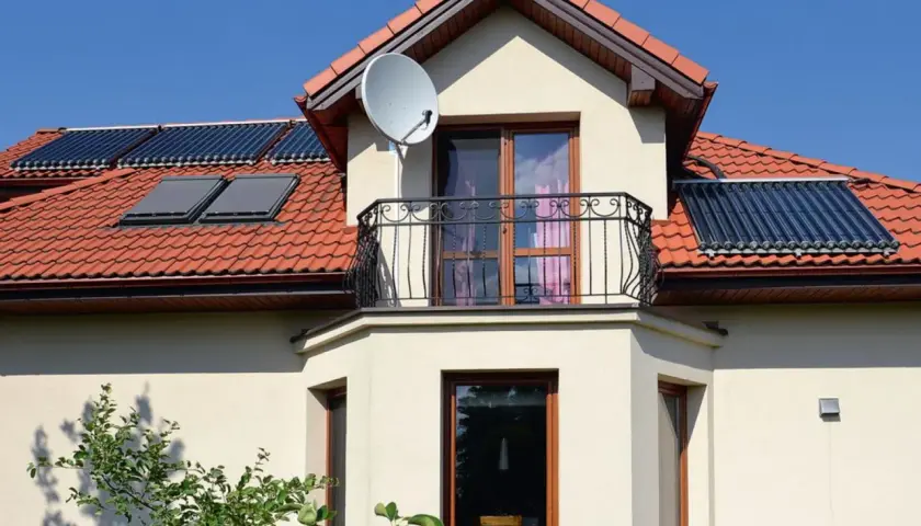 Dom z balkonem i oknami, na dachu kolektory słoneczne. Czy to wykusz co to? Tak, to element architektoniczny.