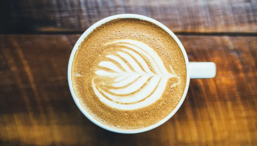Un cappuccino con latte art su un tavolo di legno. Chissà chi ha inventato il cappuccino, ma questa tazza è perfetta.
