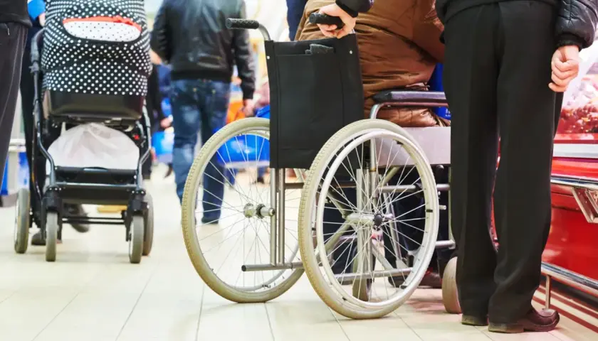 Opiekunowie osób niepełnosprawnych, wspierani przez 500 plus, poruszają się po sklepie. Wózek inwalidzki i spacerowy obok.