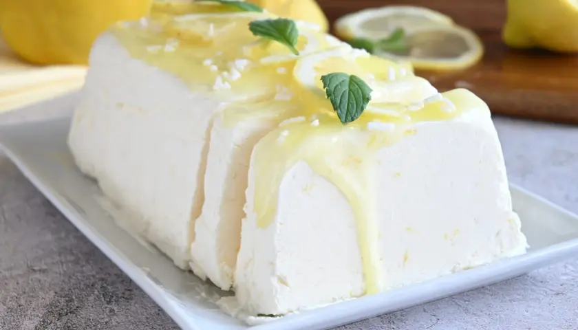 Un delizioso semifreddo al limone, guarnito con scorzette, menta e una glassa gialla, pronto per essere gustato.