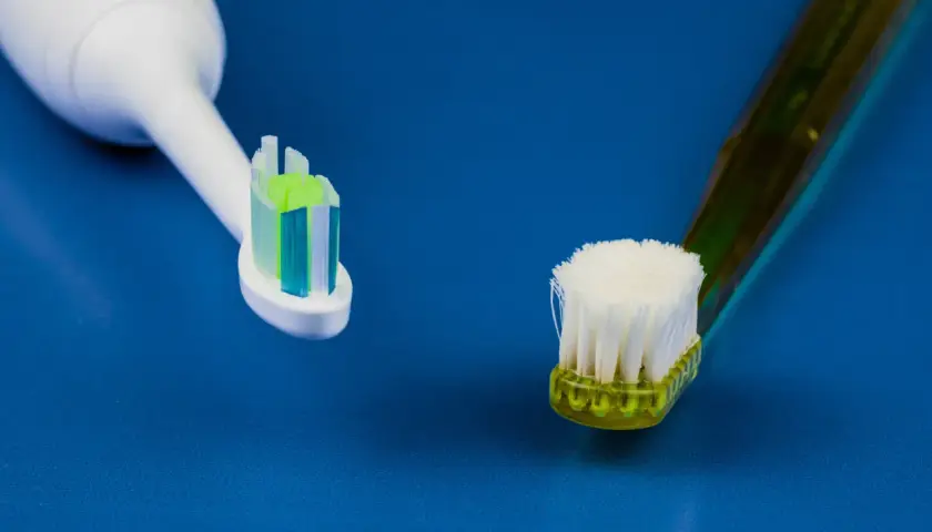 Głowica szczoteczki sonicznej obok zużytej szczoteczki manualnej na niebieskim tle.