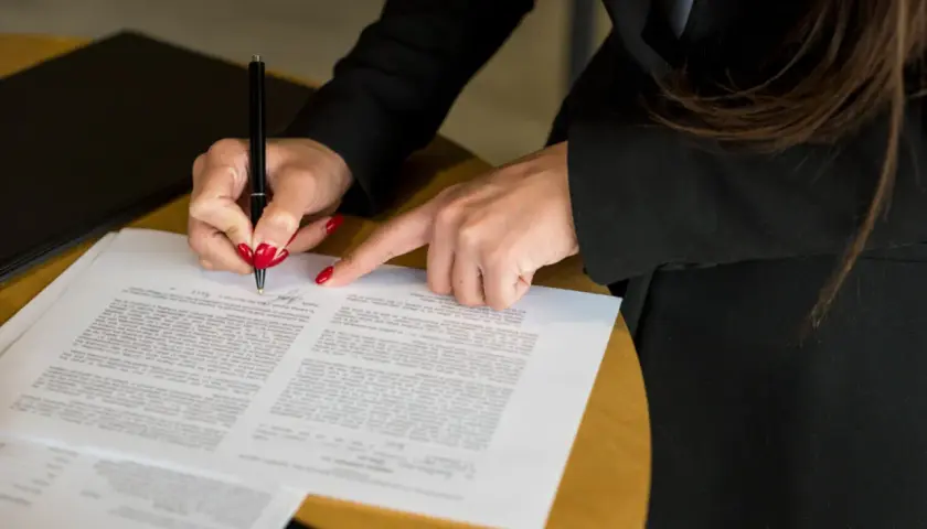 Dłoń z czerwonymi paznokciami podpisuje dokument. Może to dotyczyć hipoteki przymusowej a licytacji komorniczej.