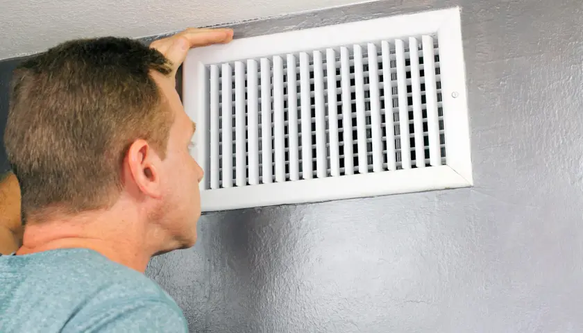 Hombre revisa un conducto de ventilación, mostrando diferentes tipos de rejillas para el aire acondicionado.