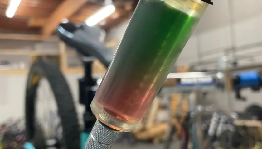 A syringe filled with red and green synthetic brake fluid, indicating a potential compatibility issue during a bike maintenance task.