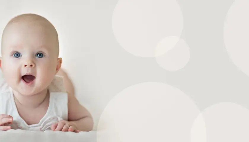 Uśmiechnięte, 4 miesięczne dziecko z niebieskimi oczami leży na brzuchu, patrząc z zaciekawieniem.