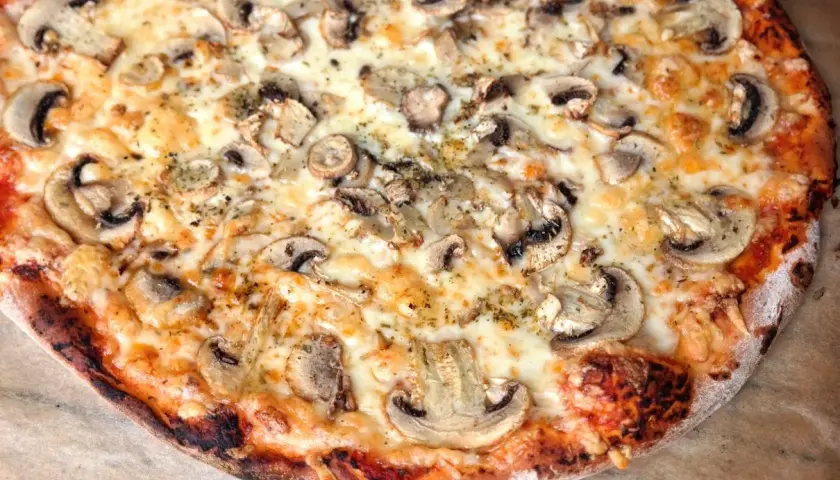 Pyszna, gorąca pizza domowa z pieczarkami i ciągnącym się serem. Idealna na wieczór filmowy.