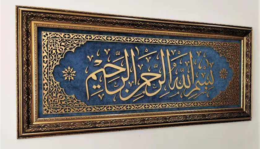 Złota kaligrafia "Bismillah" na granatowym tle, w bogatej, zdobionej ramie.