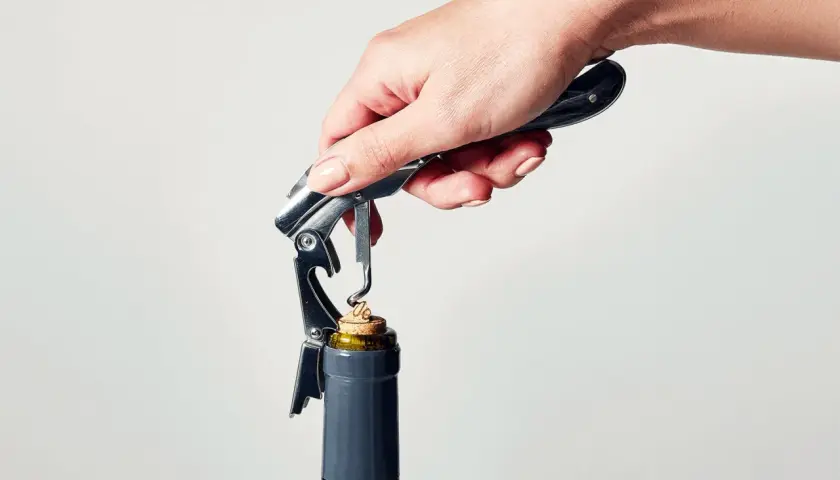 En hand använder en korkskruv för att öppna en vinflaska. Korkskruven har en metallspiral som liknar korkskruvar hår.