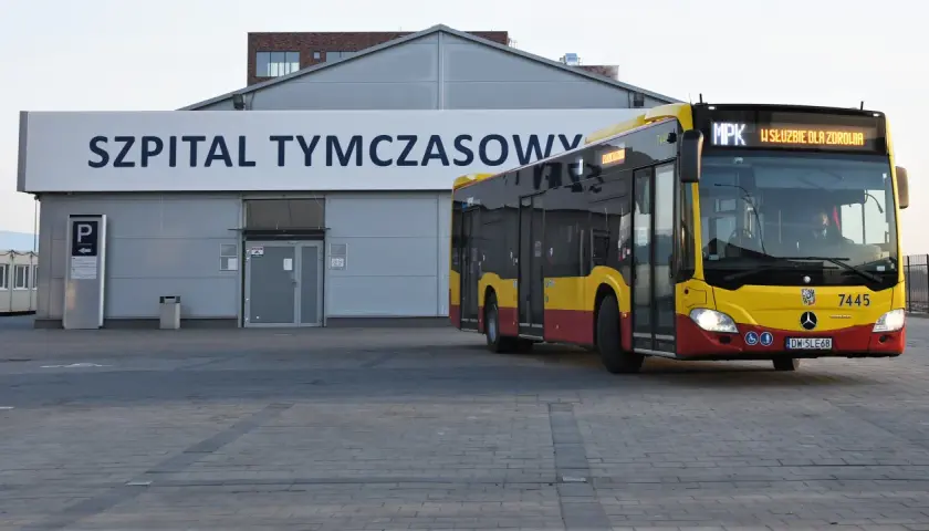 Żółto-czerwony autobus MPK z napisem "W SŁUŻBIE DLA ZDROWIA" dojeżdża do Szpitala Tymczasowego we Wrocławiu przy ul. Borowskiej.