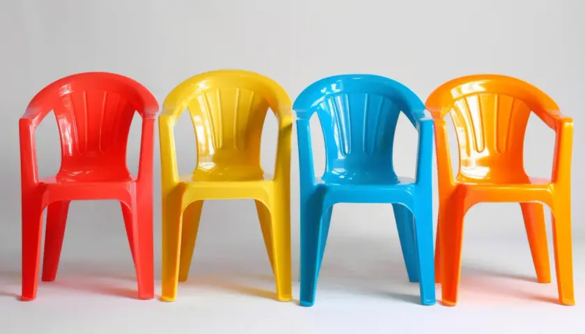 Cztery kolorowe plastikowe krzesełka: czerwone, żółte, niebieskie i pomarańczowe. Idealne do ogrodu, zastanawiasz się, czym pomalować plastik?