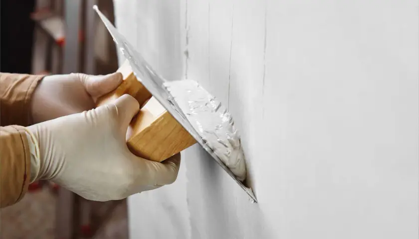 Manos con guantes aplican yeso a una pared. Pregúntate: cuanto tarda el yeso en secar para poder pintar.