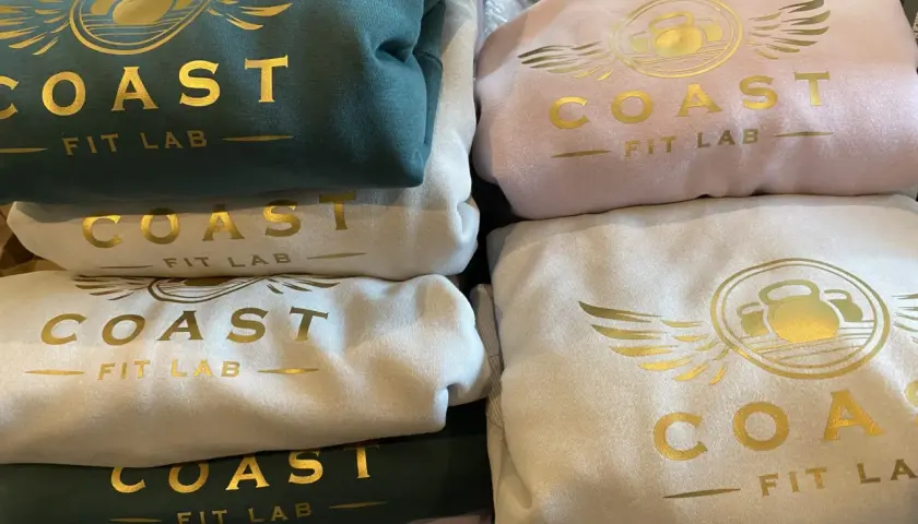 Stosik bluz klubowych w kolorach zielonym, różowym i kremowym, z złotym logo "COAST FIT LAB".