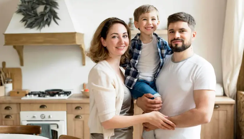 Uśmiechnięta rodzina: ojciec trzyma syna, matka obejmuje ich.