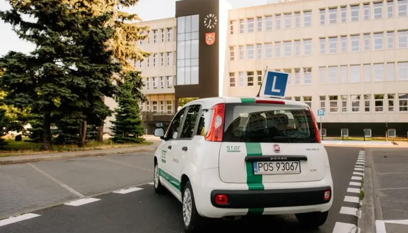 Biały Fiat Panda z zielonym pasem i literą "L" na dachu, gotowy do nauki jazdy. To auto jest kluczowe, gdy zastanawiasz się, co jest potrzebne do odbioru prawa jazdy.