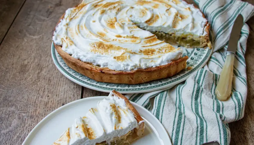 Tarte à la rhubarbe sur pâte feuilletée, recouverte d'une meringue dorée. Une part est servie sur une assiette.