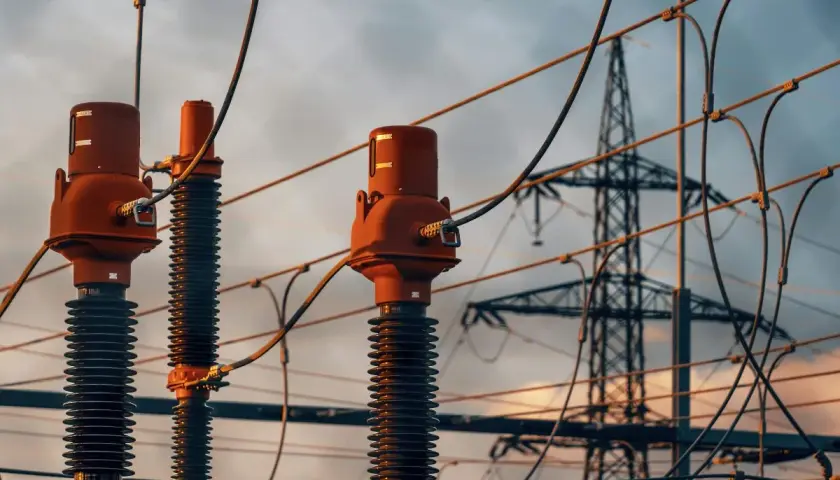 Zbliżenie na izolatory i przewody linii energetycznych. W tle widoczna wieża przesyłowa. Tabela odległości od linii energetycznych napowietrznych jest kluczowa dla bezpieczeństwa.