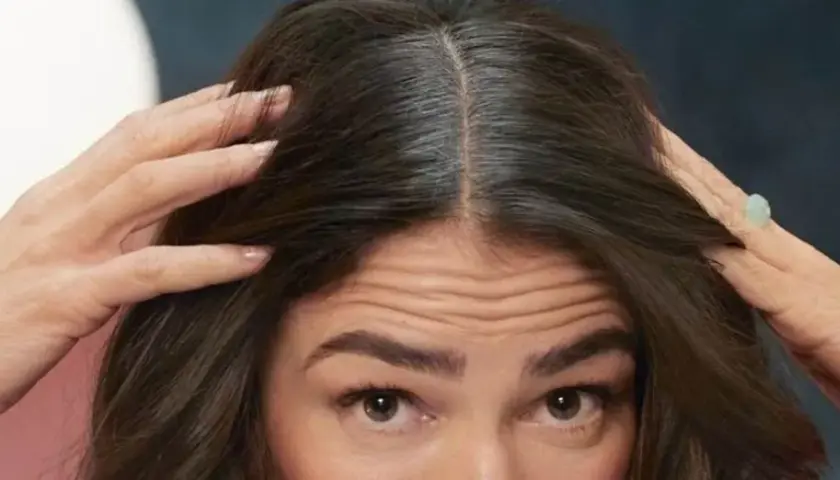 Mujer revisa su cabello oscuro con algunas canas. ¿Buscas como eliminar las canas para siempre?