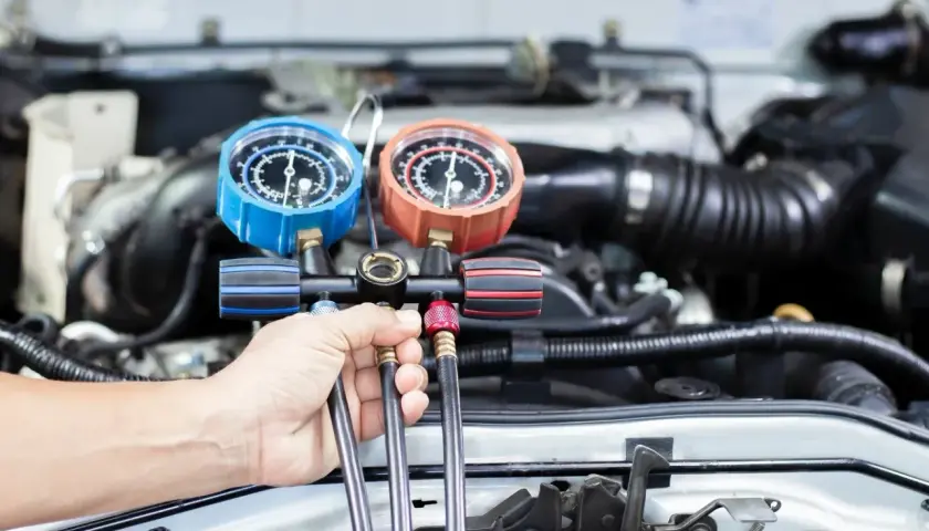 Mechanik sprawdza ciśnienie czynnika r1234yf w układzie klimatyzacji samochodu za pomocą manometrów.