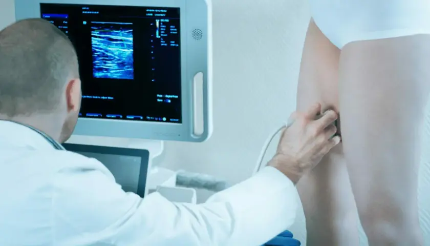 Lekarz wykonuje doppler żył kończyn dolnych, analizując obraz na monitorze.