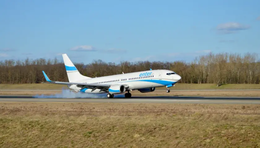 Samolot Enter Air ląduje na pasie startowym, wzbijając tumany kurzu.
