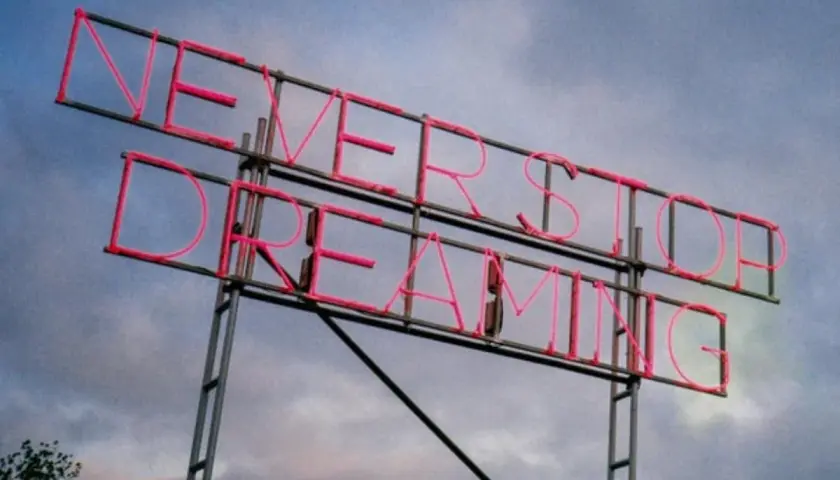 Insegna al neon rosa con la scritta "NEVER STOP DREAMING". Un promemoria ispiratore, come frasi sulla rinascita in inglese, per non smettere mai di sognare.