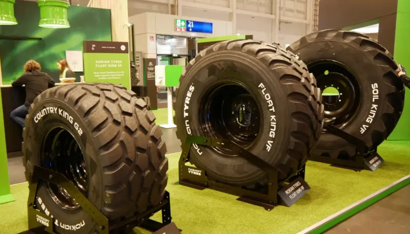 Trzy duże opony rolnicze Nokian Tyres na zielonej wykładzinie.