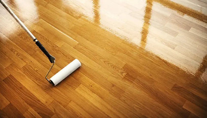 Rodillo aplicando barniz para limpiar parquet y darle un acabado brillante.