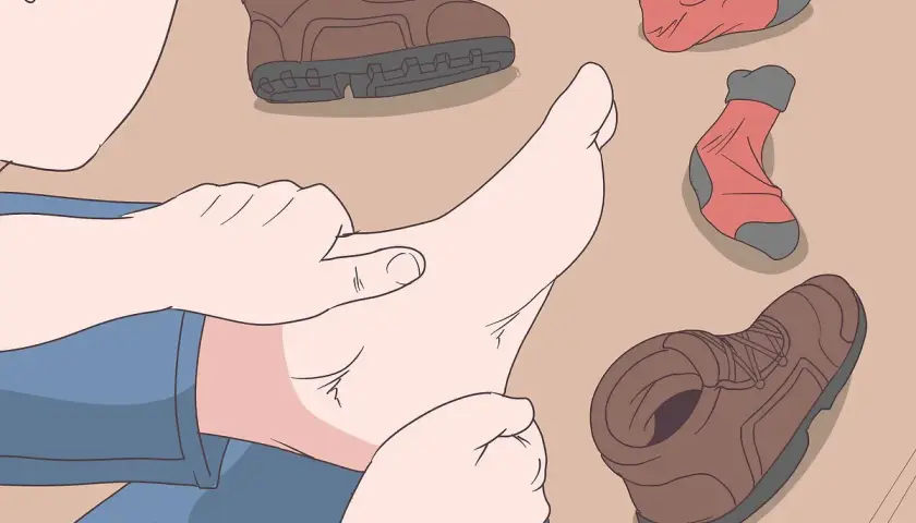 A person checks their foot, surrounded by hiking boots and socks, to prevent walking boots rubbing above the ankle.