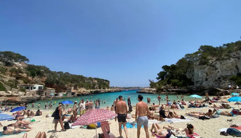 Słoneczna pogoda na Majorce, plaża pełna ludzi kąpiących się i opalających.