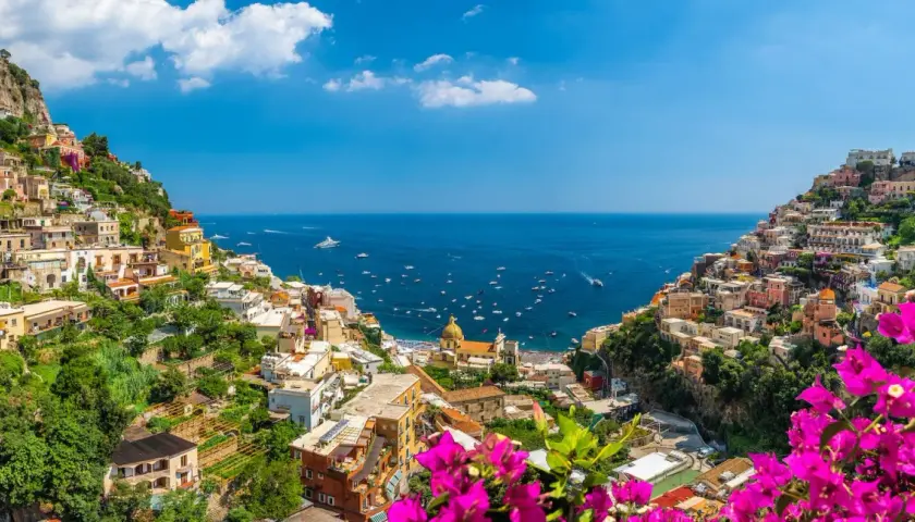 Colorful houses cascade down a cliffside to the sea, a picturesque view of the Amalfi Coast, a popular destination from Naples Airport.