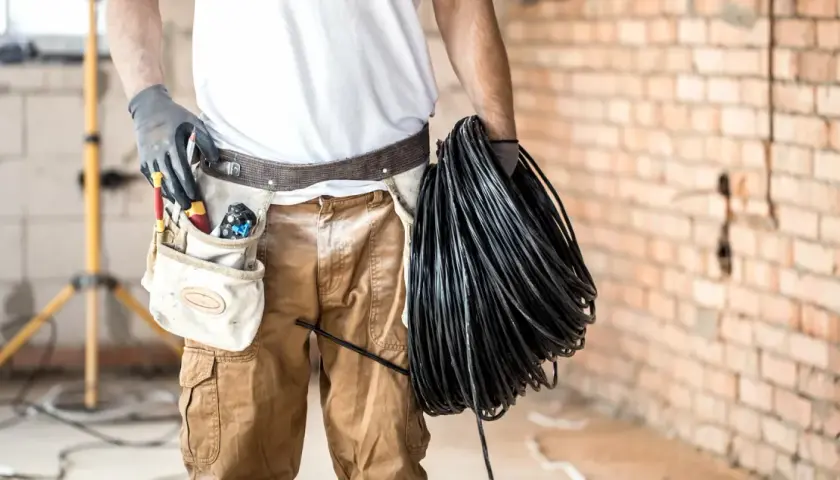 Elektryk z narzędziami w pasie trzyma zwój czarnego kabla. Czy będzie układany w peszlu, czy bezpośrednio w ziemi?