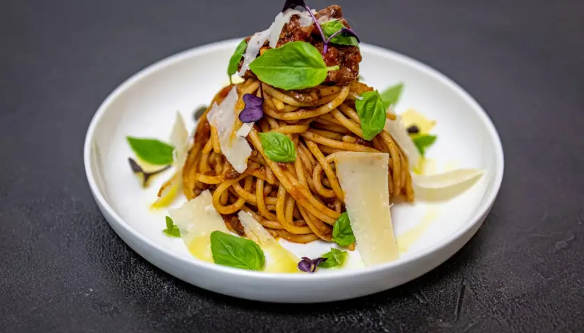 Pyszne spaghetti alla norma z sosem pomidorowym, bakłażanem, bazylią i parmezanem, podane na białym talerzu.