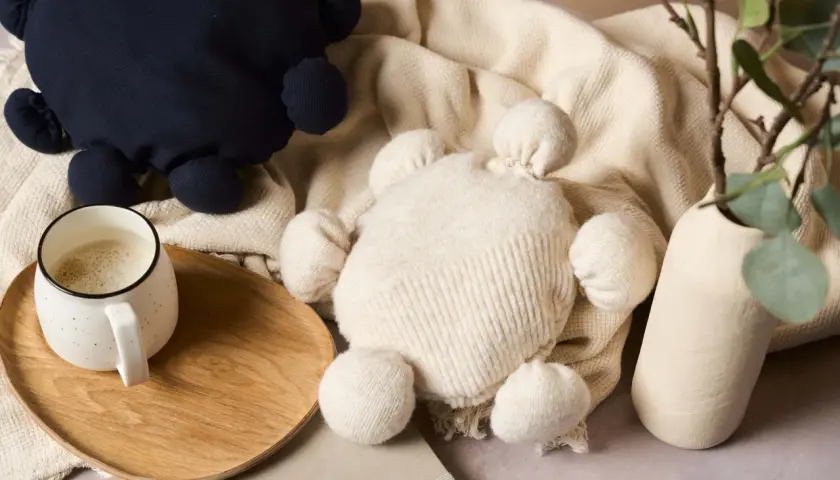 Zwei Kuscheltiere, eines dunkelblau, das andere cremefarben, liegen auf einer Decke. Ein Becher Kaffee steht auf einem Holztablett. Kreatives **Pullover Upcycling** für süße Spielzeuge.