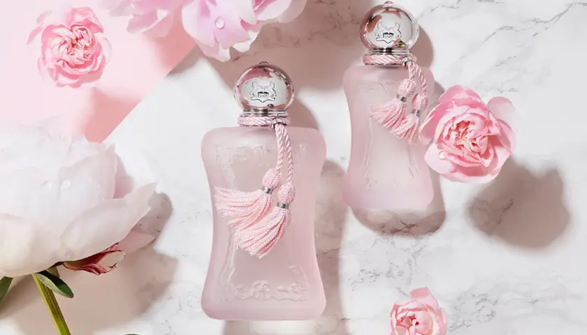 Dwa różowe flakoniki perfum de marly delina otoczone delikatnymi różowymi kwiatami i piwoniami.