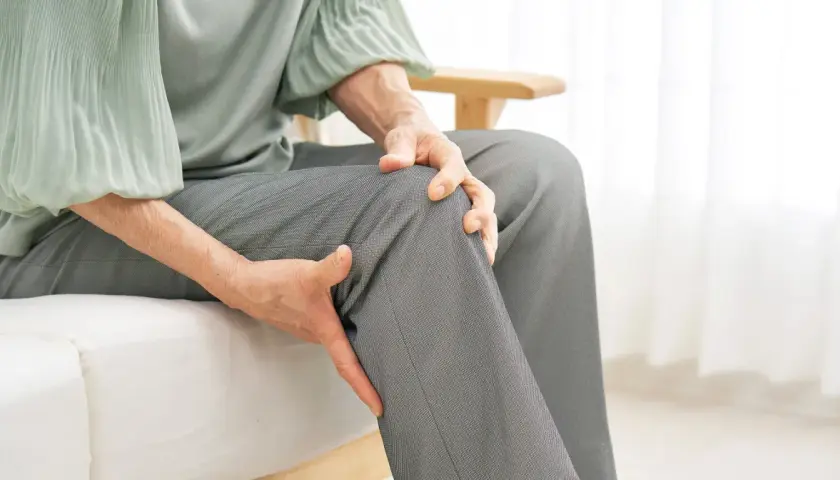 Osoba w średnim wieku trzyma się za kolano, szukając ulgi. Czy glukozamina co to i jak może pomóc?