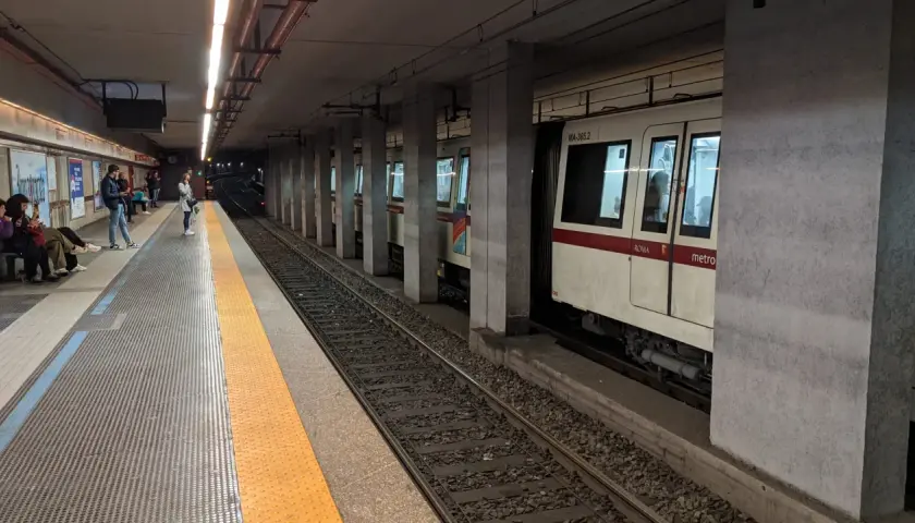 Persone attendono il treno alla stazione metro a Lepanto. Un convoglio bianco e rosso è fermo sui binari.