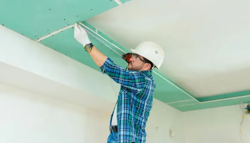 Operaio con casco misura il soffitto in cartongesso, pronto per lo stucco.