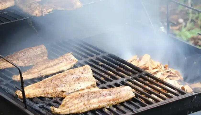 Poisson fumé sur un gril, avec des copeaux de bois qui dégagent de la fumée. Idéal pour savoir quel bois pour fabriquer un fumoir.