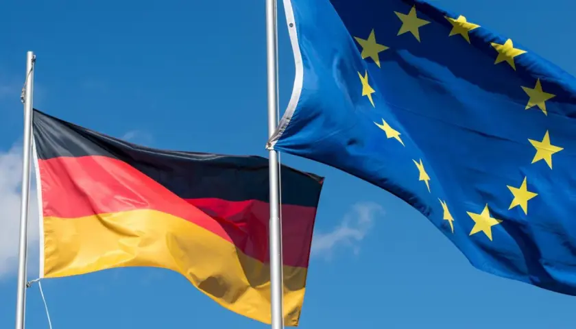 Die deutsche und die EU-Flagge wehen im Wind vor blauem Himmel.