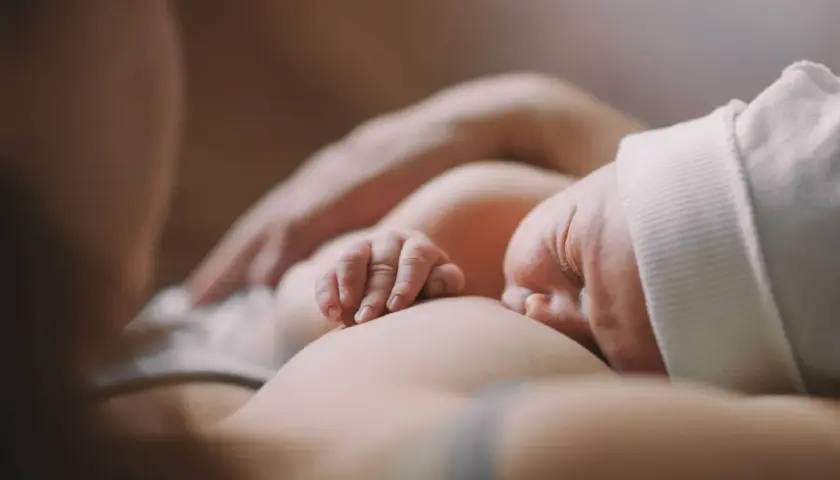 Delikatne dłonie noworodka obejmujące pierś podczas karmienia. Ulewanie u noworodka to częsty widok, ale ten moment to czysta bliskość.
