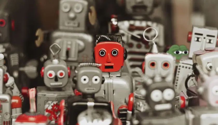 Kolekcja robotów zabawek, w tym jeden czerwony z przerażonym wyrazem twarzy, przypomina teorię martwego internetu.