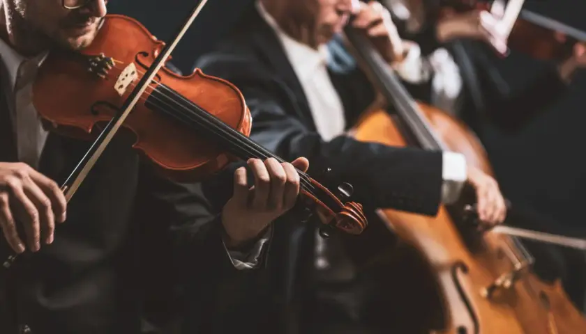 Muzycy w eleganckich strojach grają na instrumentach smyczkowych. W centrum uwagi skrzypek, a w tle wiolonczela. To piękny intro do koncertu.