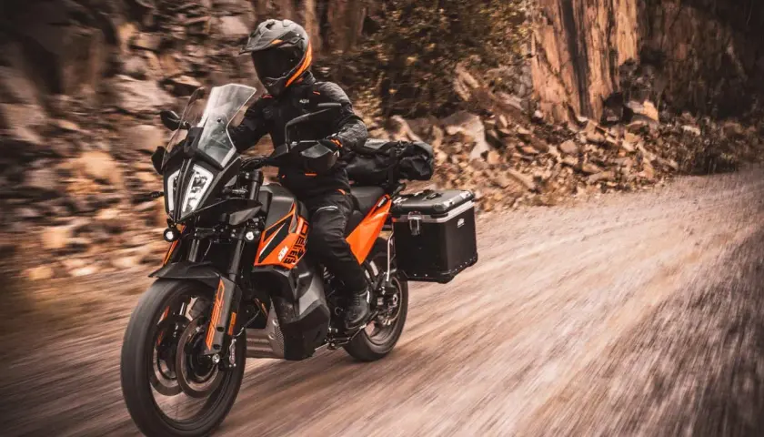 Motociclista en KTM naranja y negra, equipada para aventura, recorre un camino de tierra. La mejor moto trail media cilindrada lista para la exploración.