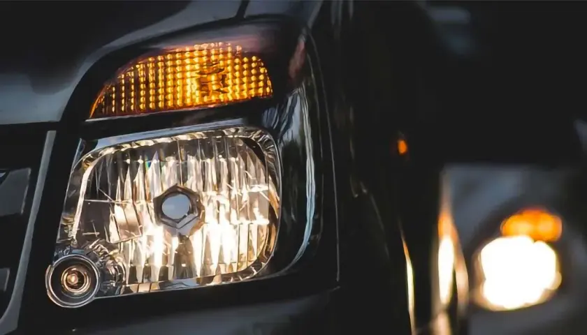 Luces cruce de un coche, con el intermitente naranja encendido y el faro principal iluminando. Otro coche se ve al fondo.