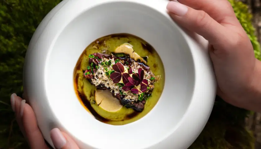 Wykwintne danie z restauracji z gwiazdką Michelin, podane w białej misie na tle mchu.