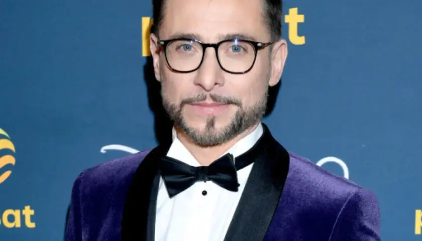 Kacper Kuszewski w fioletowym aksamitnym garniturze z czarną muszką. Wygląda elegancko, jakby wybierał się na galę z żoną.