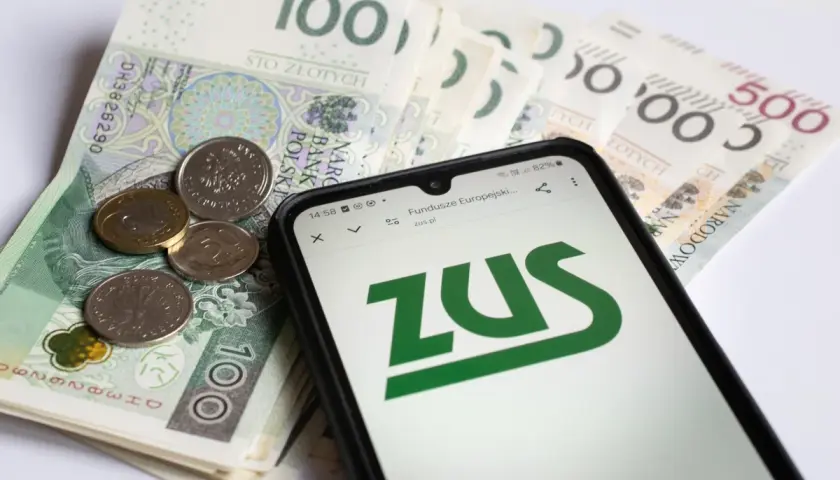 Pieniądze i telefon z logo ZUS. Ojciec planuje urlop rodzicielski, sprawdza świadczenia.