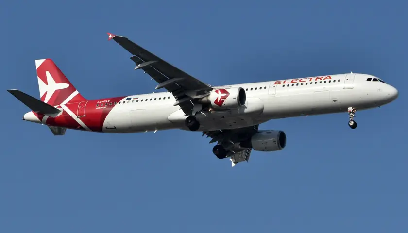 Samolot linii lotniczych Electra Airways z czerwonym ogonem i białym kadłubem leci na tle błękitnego nieba.