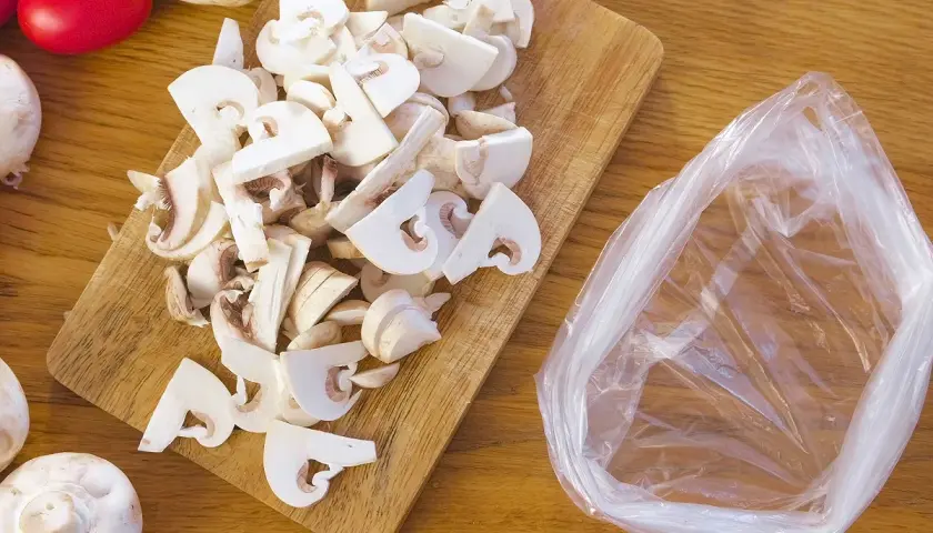 Champignons frais coupés sur une planche en bois, prêts à être mis dans un sac pour apprendre comment congeler des champignons frais.