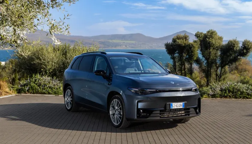 Leapmotor B10 REEV, un SUV elettrico dal design moderno, parcheggiato su un selciato con vista su un lago e colline verdi.